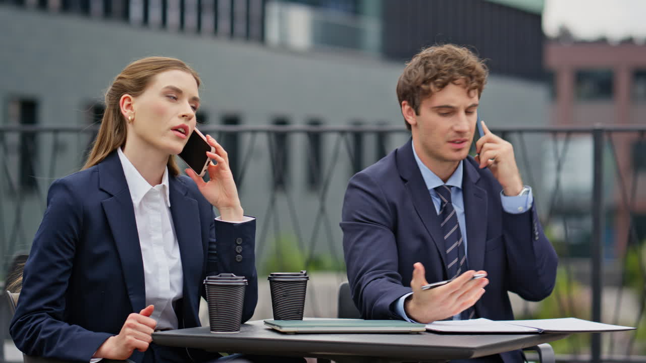 Worried coworkers negotiating phone call sitting outdoors restaurant closeup