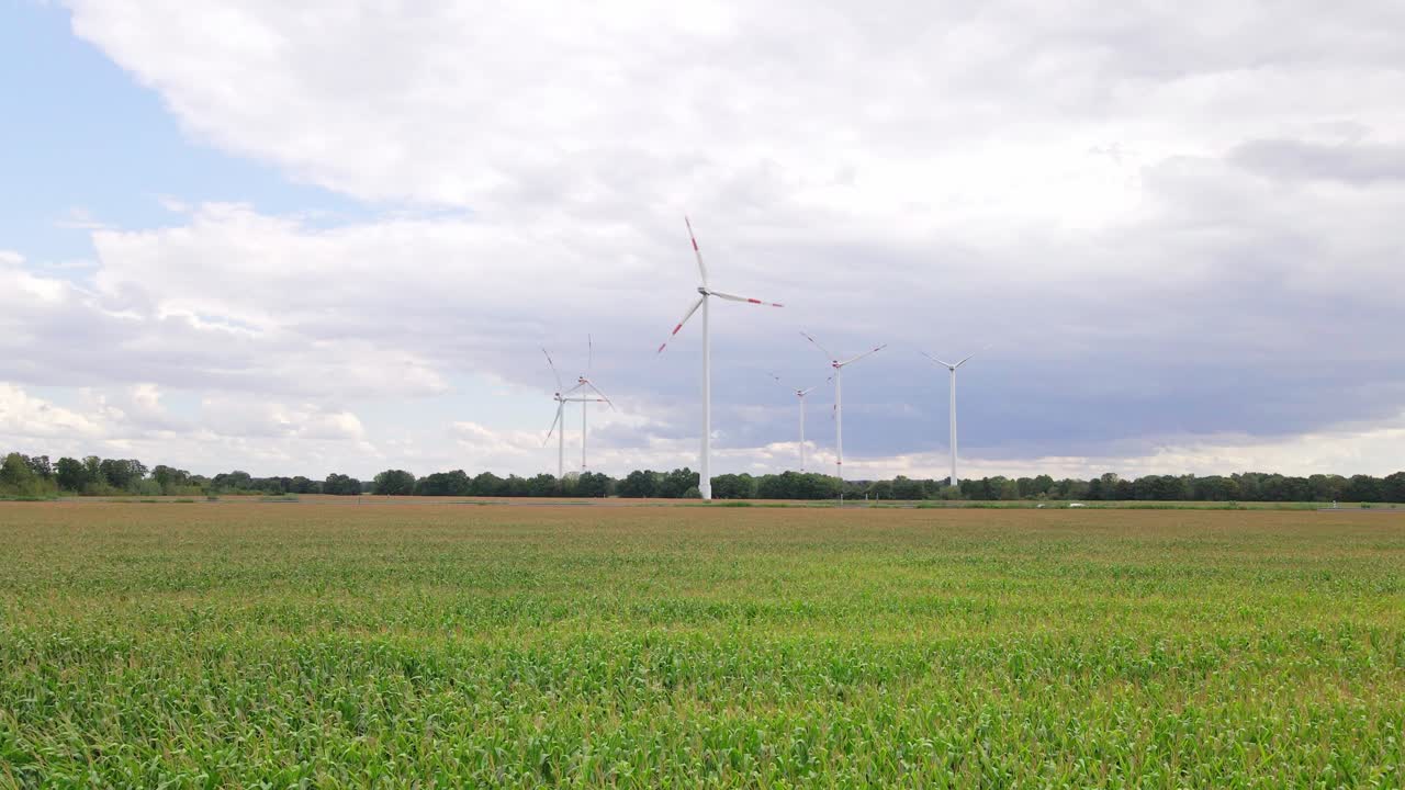 Drone footage of wind turbines beside a highway, surrounded by farmland and cornfields