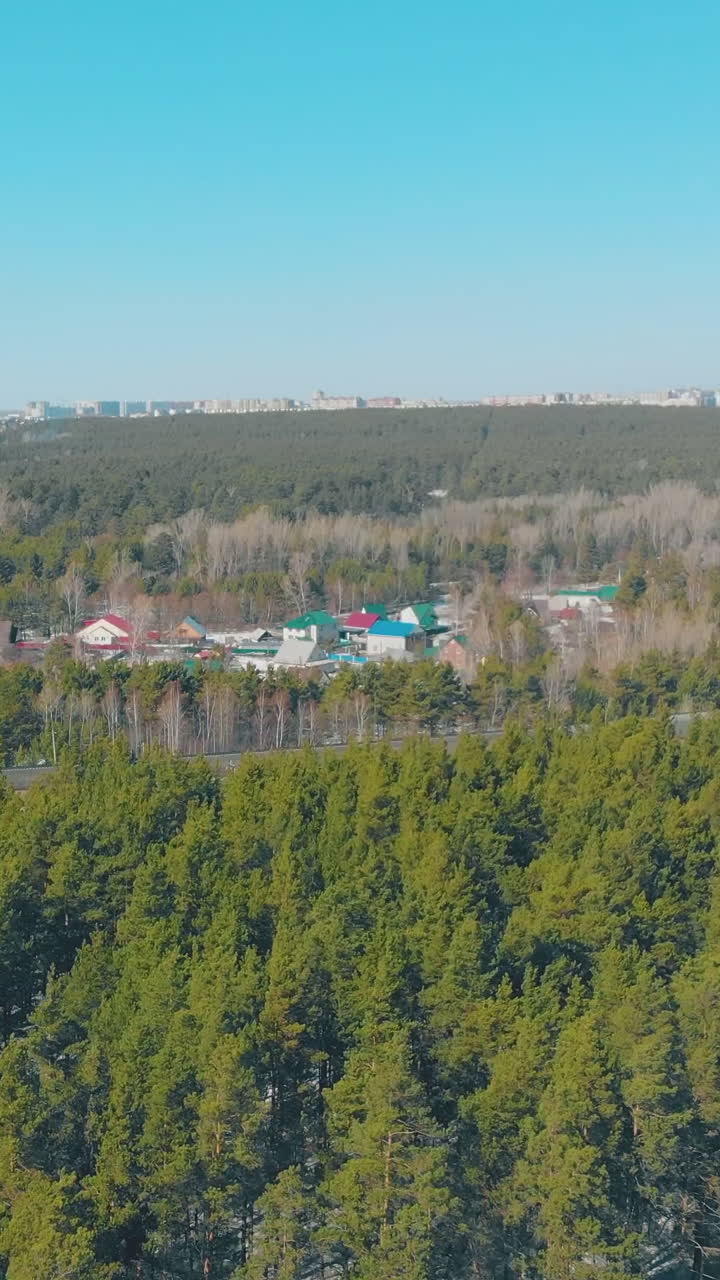 grey winding roads and evergreen pine forests surround cottage village buildings against city silhouette upper view