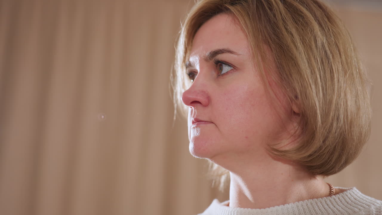 Close up of thoughtful woman in soft sweater gently lifting head with calm expression while listening attentively during therapy session in warm indoor space with soft lighting and neutral curtains