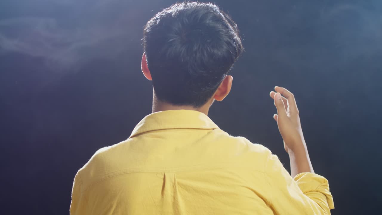 젊은 아시아 소년이 마이크를 들고  연기 검은 배경에서 노래하는 근접적인 뒷면