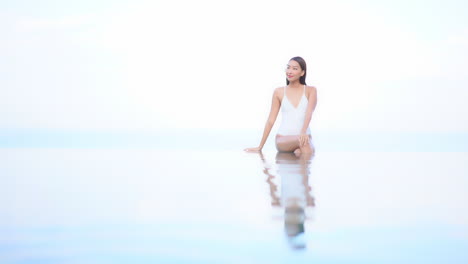 Dreamy-Tropical-Vacation,-Woman-in-Swimsuit-and-Flower-in-Hair-in-Infinity-Pool-Merging-With-Sky