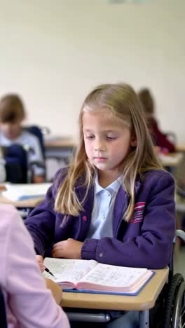 a girl in a wheelchair is sitting at a desk in a classroom