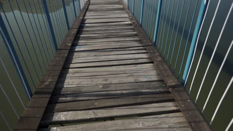 la cámara se mueve hacia adelante revelando un puente estrecho con barandillas azules de acero y tirantes sobre un cuerpo de agua turbio