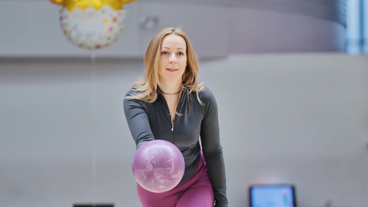 Joueuse de bowling lançant une boule violette - Vue en contre-plongée le long d'une piste de bowling polie