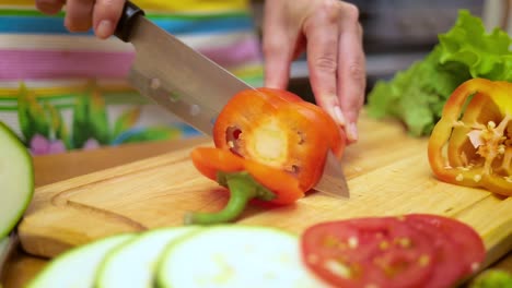 female hands of housewife with a knife cut fresh bell pepper on chopping board kitchen table