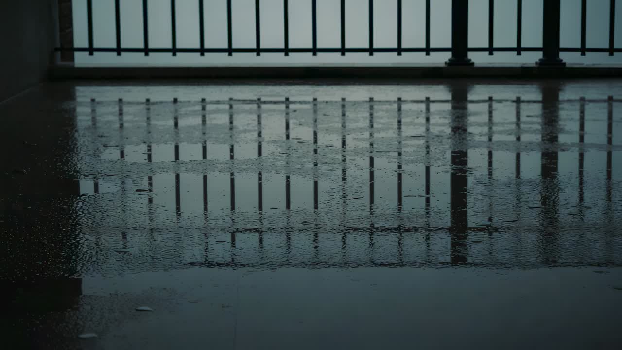 Rippling metal railing reflection warping, restoring on wet concrete floor while raindrops striking