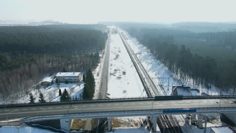 Viaducto-Vacío-Cruzando-Otra-Carretera-Negra-Y-Tres-Vías-De-Ferrocarril-Cerca-De-Una-Estación-Entre-Los-árboles-En-Un-Paisaje-Invernal-Nera-Rakowice