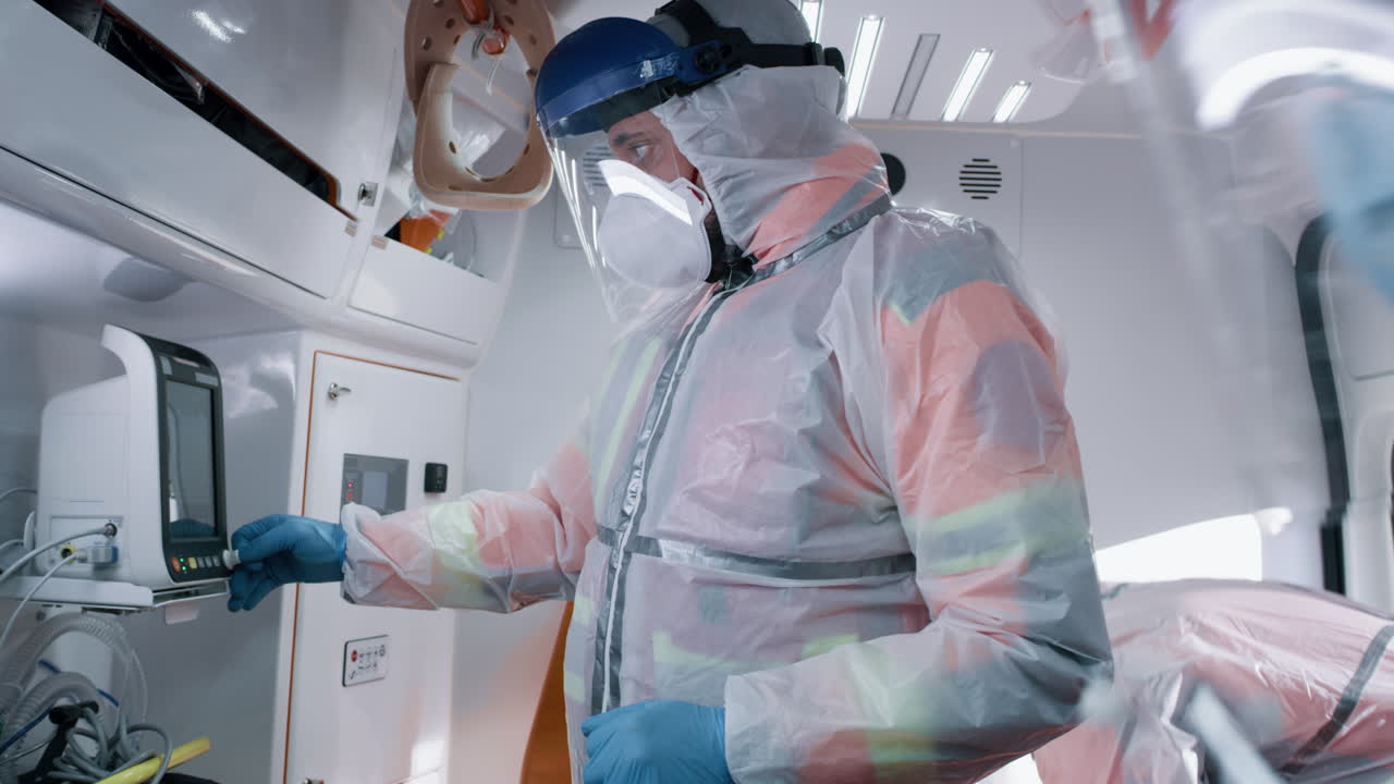paramedics Using Life Support Machine in Ambulance Team of Medical Practitioners in Hazmat Suits Using Life Support Machine to Help Patient with Coronavirus while Riding Ambulance to Hospital during Pandemic