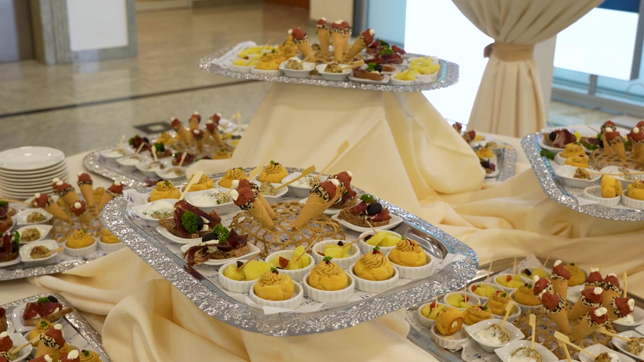 Vassoi eleganti di tartine assortite disposti su un tavolo da buffet a un evento al chiuso.