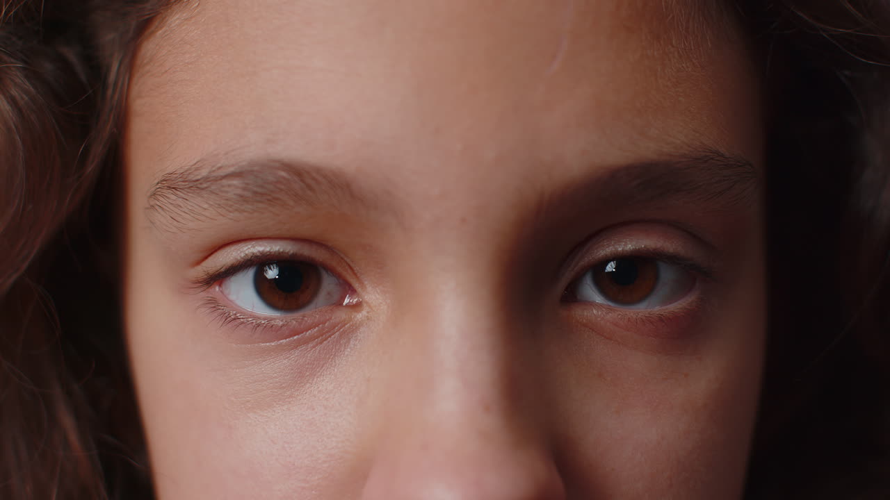 Closeup macro portrait of teen child kid face smiling brown girl eyes looking at camera blink wink