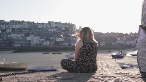 Kaukasisches-Mädchen-Sitzt-Auf-Der-Böschung-Und-Beobachtet-Die-Möwen,-Die-An-Einem-Sonnigen-Tag-Am-Hafen-In-St.-Ives,-Cornwall,-England,-Vereinigtes-Königreich,-Fliegen