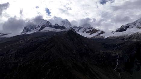 cinematic aerial view of snowy andes mountains in peru with glaciers, rocky cliffs, and hidden blue alpine lake under misty clouds, dramatic landscape and natural travel destination