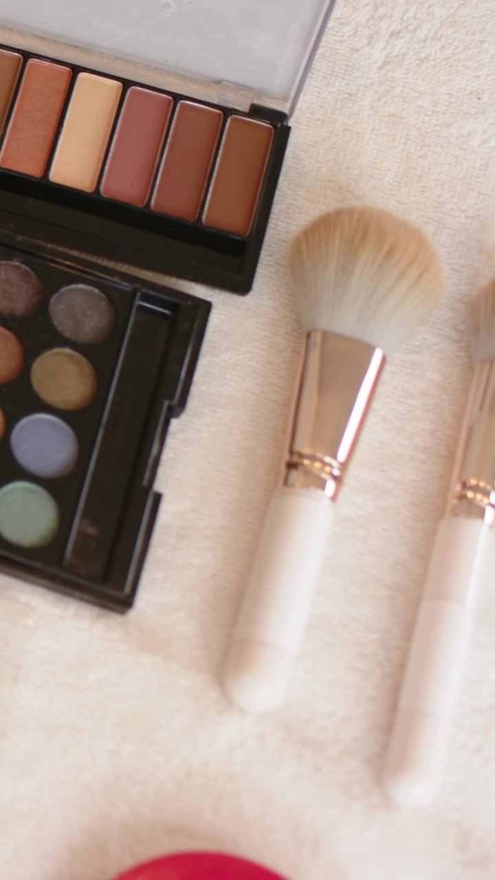Vertical video: Panning camera showing brushes on towel, revealing palettes, blush, false lashes