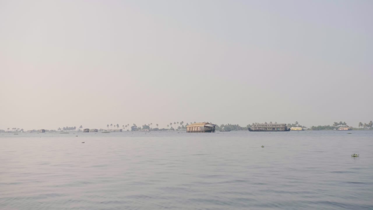 더 넓은 케랄라 백워터에서 늦은 오후 태양 아래 멀리 몇 척의 하우스보트를 볼 수 있습니다.