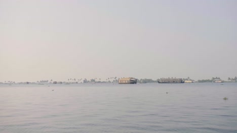 On-a-wider-expanse-of-kerala-backwaters-several-houseboats-can-be-seen-in-the-distance-in-the-late-afternoon-sun