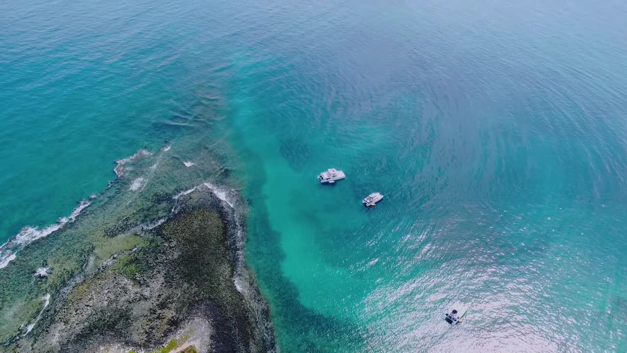 Arcipelago di Abrolhos che mostra splendide formazioni di barriera corallina, acqua cristallina turchese e barche che navigano nel vivace ecosistema marino in Bahia, Brasile, con ripresa aerea dall'alto che scivola e rivela