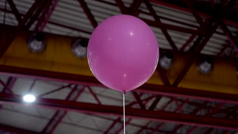 single pink balloon suspended inside large industrial space