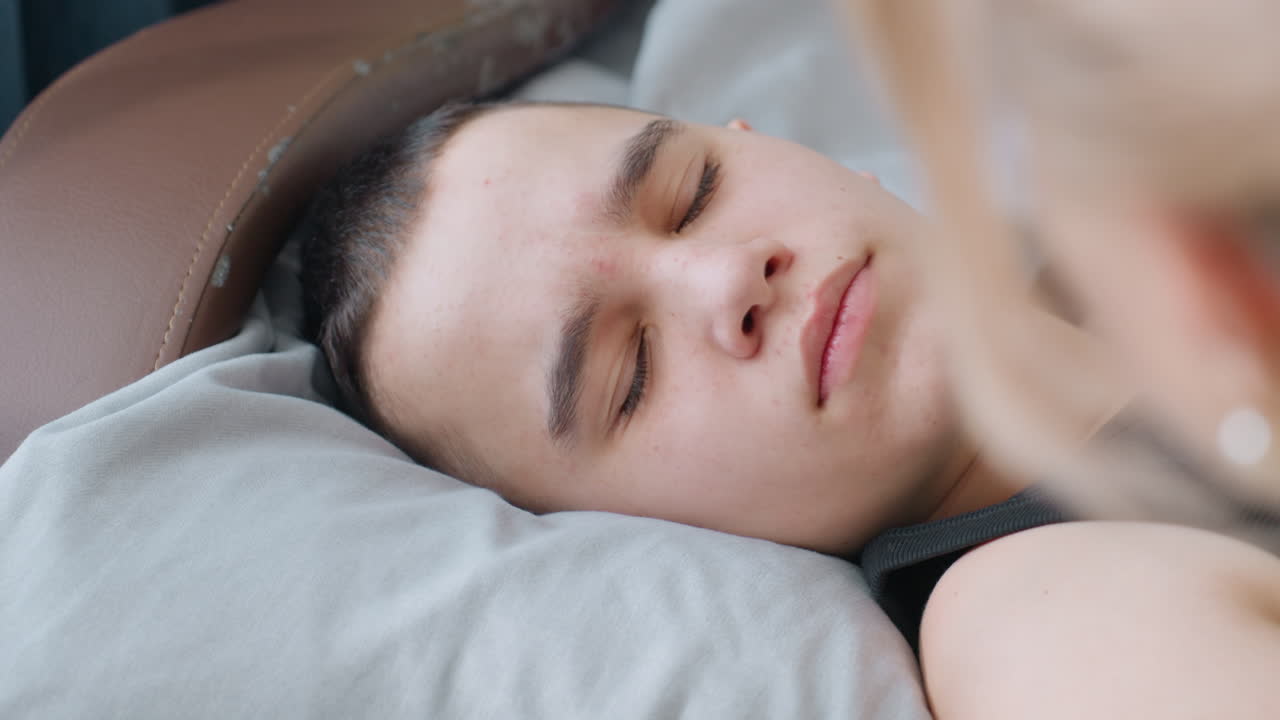 Close up hand view of mother with polished nails gently touching nose of son sleeping on pillow as he slowly opens eyes with warm smile showing care and affection
