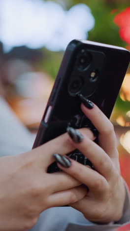 블랙 폴리시드 손을 가진 여성이 전화로 대화하는 클로즈업, 부드러운 활기차고 흐릿한 배경에 보케 빛이 특징으로, 우아한 설정에서 세련되고 현대적인 커뮤니케이션 순간을 보여줍니다.
