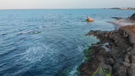 Aerial-shot-with-drone-rising-over-seashore-cliffs-and-houses-in-background-at-sunset