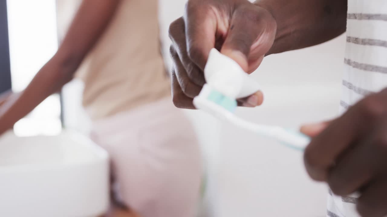 Midsection of african american couple brushing teeth together in bathroom, copy space, slow motion