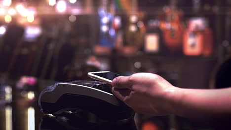 a man using mobile phone to purchase product at the point of sale terminal in a retail store with near field communication for verification to complete the sale transaction