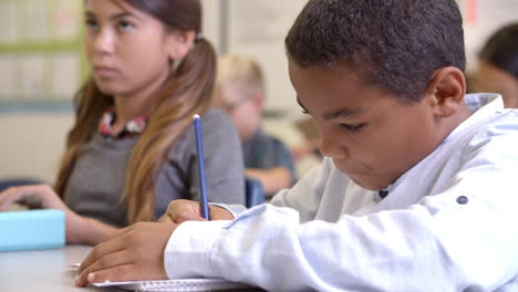 primer plano de un estudiante de quinto grado escribiendo en su escritorio en clase