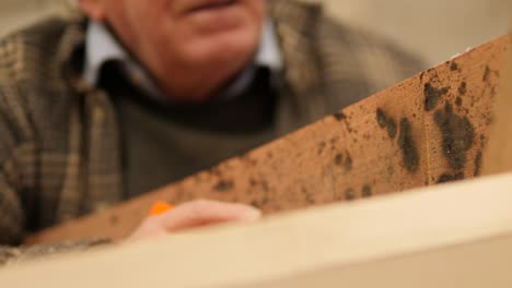An older, experienced boatbuilder takes measurements while building a wooden boat