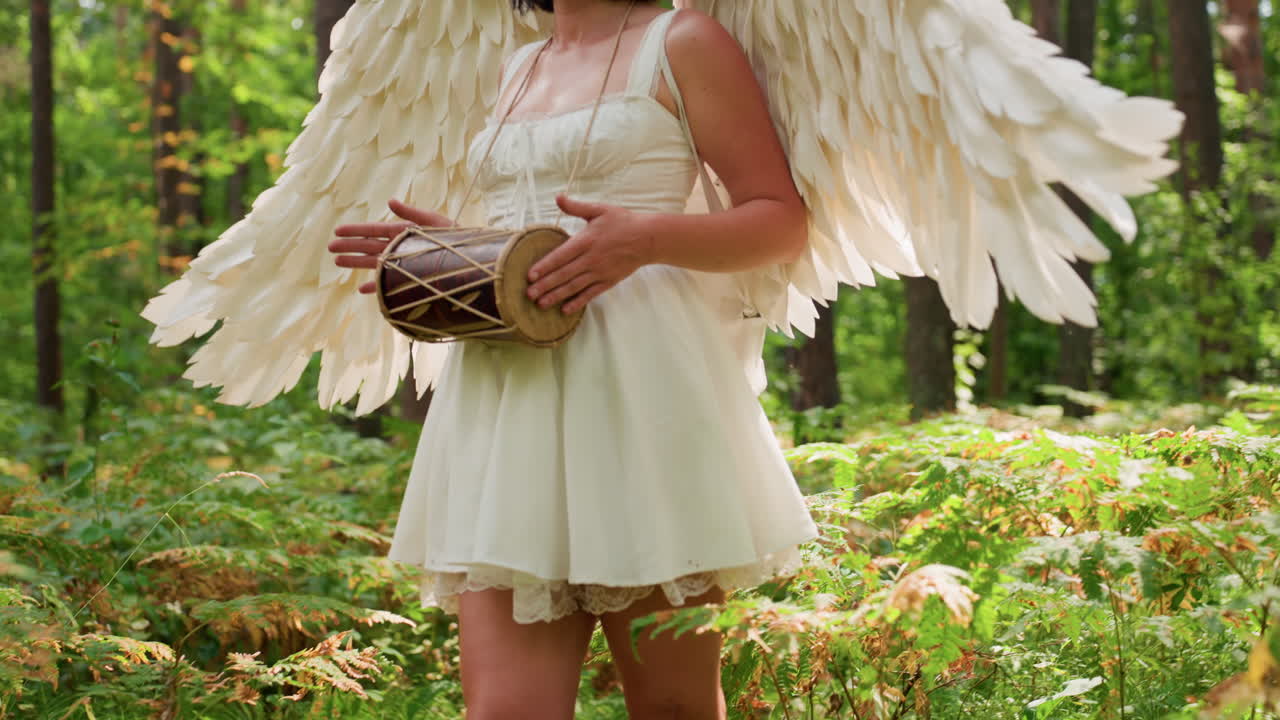 Fairy goddess with white angel wings standing in lush green forest playing kalimba, sunlight gently illuminating her serene face and flowing dress, radiating peace