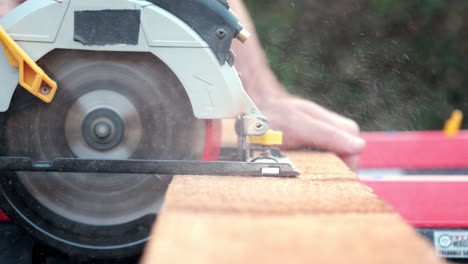 close up slow motion shot of electric power saw slicing through plank of wood outside