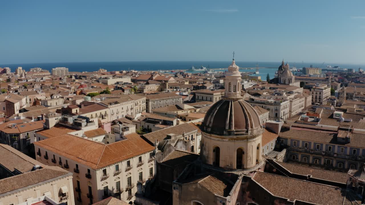 Aerial drone flight along Cathedral tower in the heart of Catania old town. Historical city of Sicily. Mediterranean sea in the background. UNESCO World heritage site.