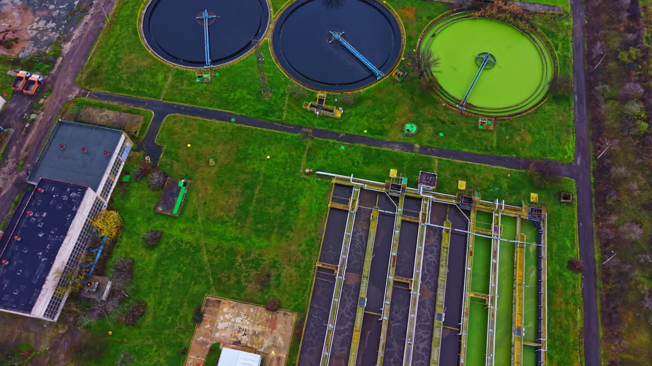 View of a water treatment facility with processing tanks and green areas in a rural setting during daytime