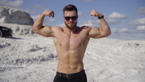 athletic man shows his muscular body outdoors. portrait of a shirtless sportsman with trained body on white canyon background in sunny daytime.