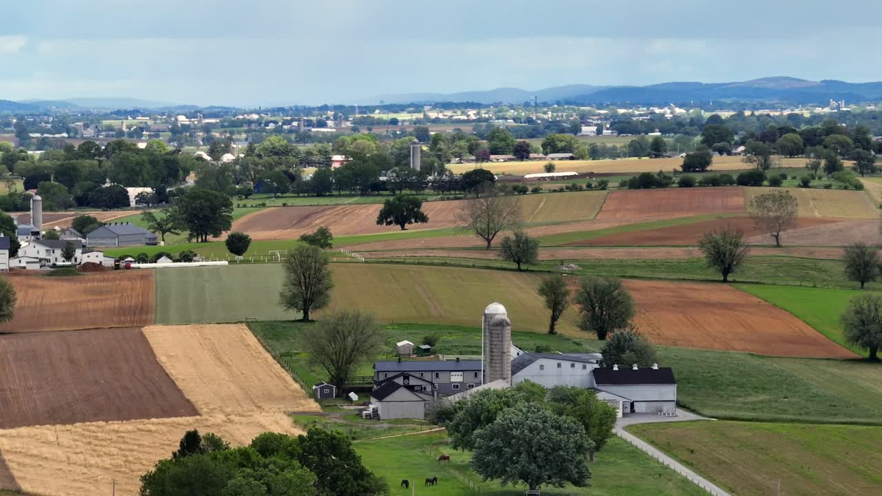 Colored hills farm fields between farmsteads in Midwest of USA. Aerial wide shot. Sunny day in America.