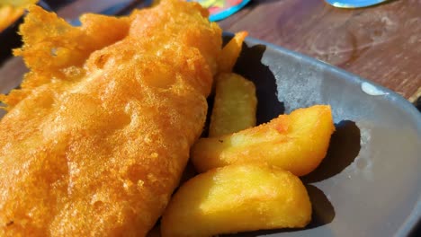 close up details of battered classic rustic british fish and chips outside during summer time. traditional fast food cuisine.