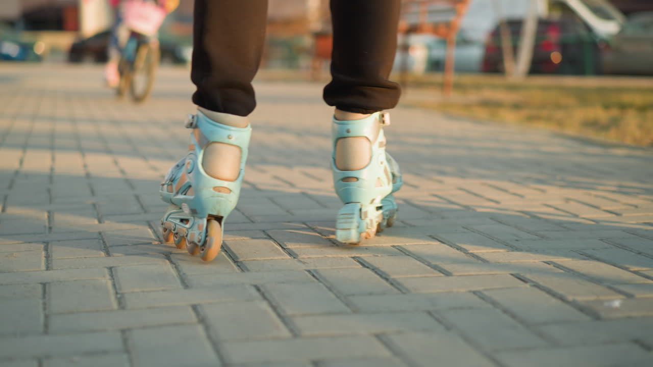 Close-up back shot of a person s feet wearing rollerblades, gliding smoothly along a paved path in a park during sunset. The golden light enhances the scene, highlighting the atmosphere of a park