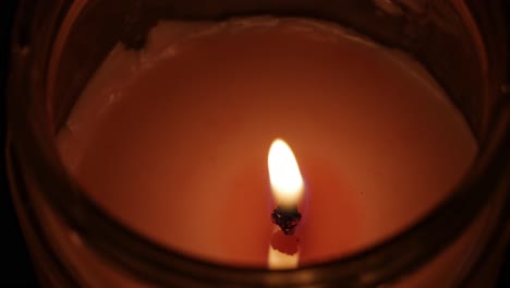 luz de velas que brilla en la oscuridad en un recipiente de vidrio con un aroma agradable y que da vida a la habitación oscura en la noche con su fuego en movimiento