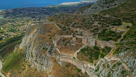 aerial drone forward moving shot over iconic archaeological site of ancient corinth built along the slope of acrocorinth, peloponnese, greece on a cloudy day