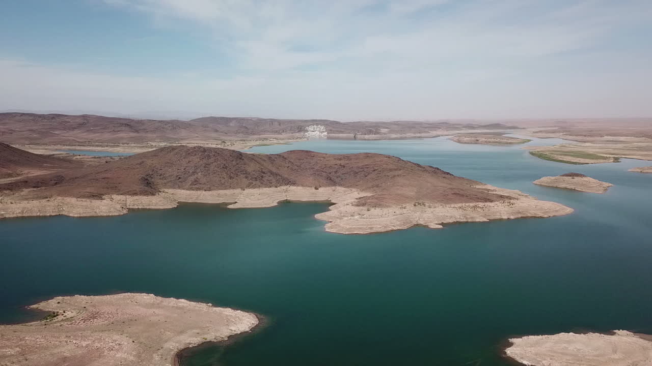 Vista aerea panoramica 4K di un enorme bacino idrico blu con numerose isole e una costa aspra e arida. Prospettiva dall'alto che mostra la sicurezza idrica e la bellezza geografica nelle regioni aride