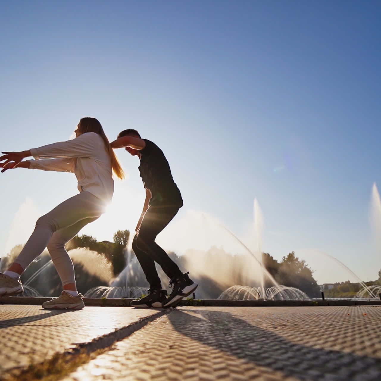 Dancers against beautiful fountain. Young couple performing a modern dance on the urban background. Contemporary freestyle dance of teens outdoors through the leaks of sun.