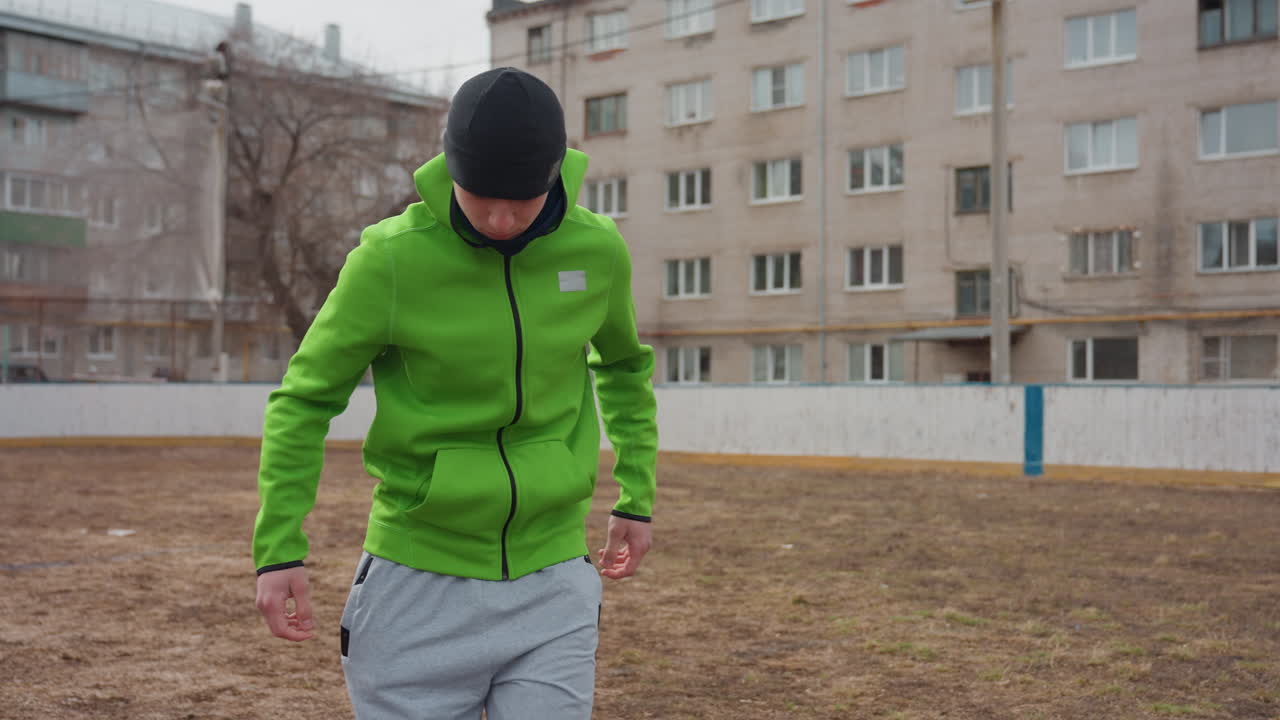 Сосредоточенный мужчина балансирует с футбольным мячом; городской житель отрабатывает технику работы с мячом во время тренировки; человек в яркой куртке умело жонглирует футбольным мячом во дворе