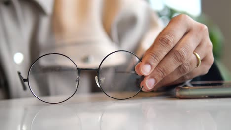 a hand reaching for and holding a pair of eyeglasses on a table