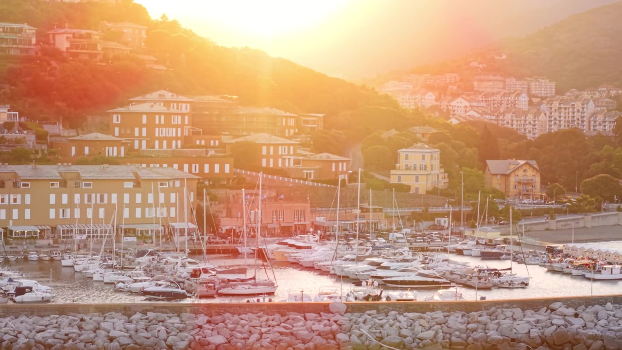 Yacht ormeggiati nel porto turistico di Arenzano con la città collinare e la calda luce del tramonto in Liguria.