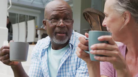 Glückliches-älteres,-Vielfältiges-Paar,-Das-Hemden-Trägt-Und-Kaffee-Im-Garten-Trinkt