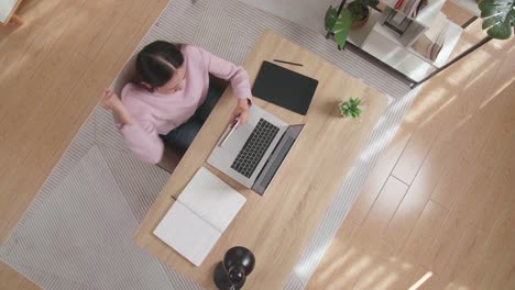 vista superior zoom out toma de una mujer celebrando el juego de wining en el teléfono inteligente mientras está sentada en el escritorio de madera en casa