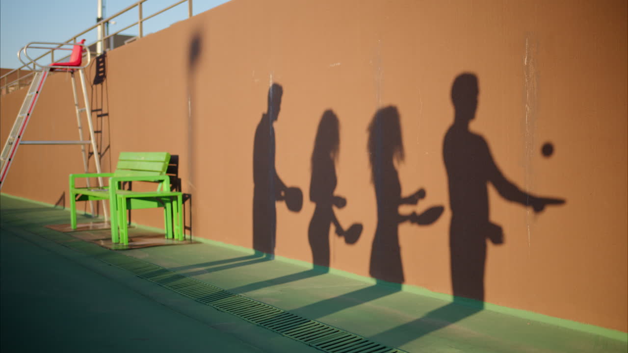 The shadow of two men and two women practicing to play pickleball on a court on a sunny day