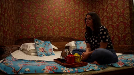 mujer cansada bostezando sentada en una cama tradicional kang con un juego de té de cerámica en china