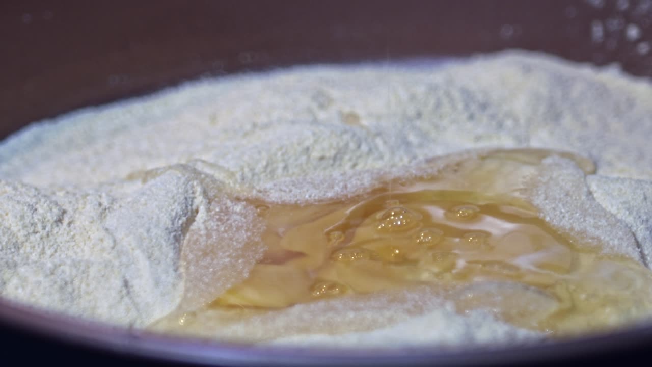 A raw egg splashes down onto a plate full of flour ready for kneading