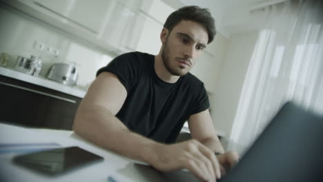 hombre serio escribiendo computadora portátil en casa. hombre de negocios usando computadora en la cocina